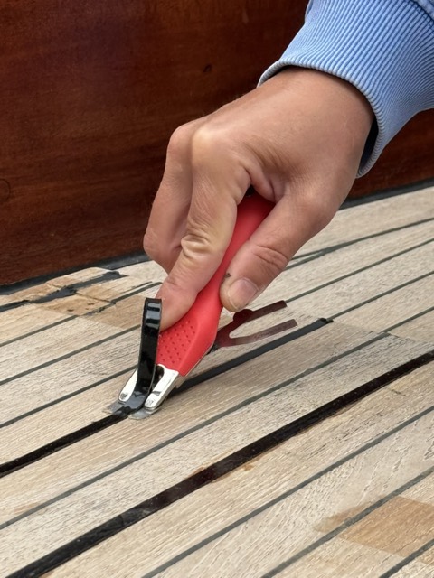 Hand zieht mit dem rot-griffigen Mozart-Messer die überstehende Fugenmasse ab