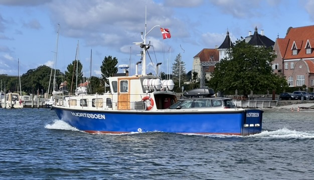 Blau-weiße Inselfähre Hjortøboen in Fahrt, dänische Flagge am Mast